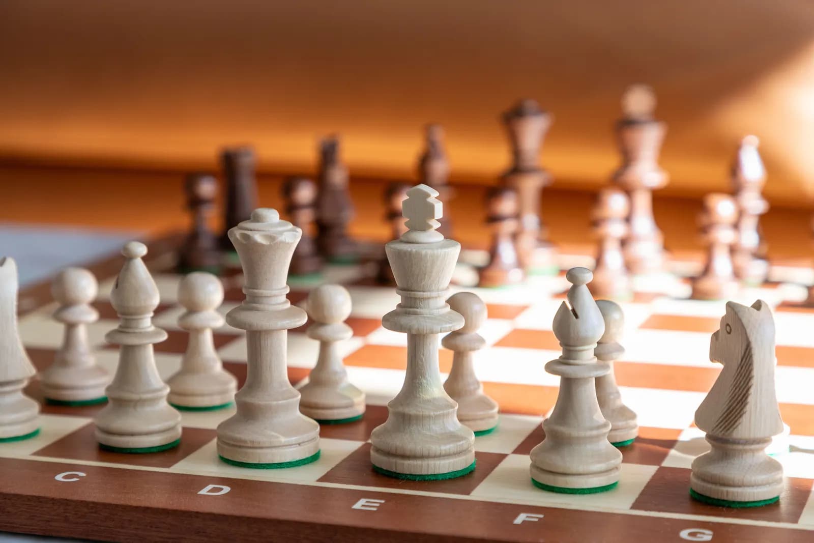 A close-up view of a chess board with the white pieces in the foreground, including the king, queen, bishop, and knight, with the dark pieces blurred in the background.